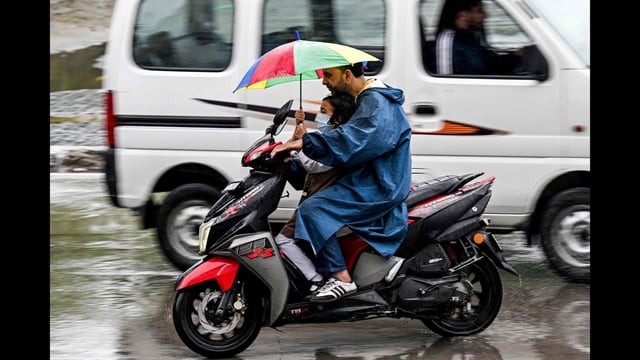 A man wearing a raincoat rides a scooter with a child during rainfall in Srinagar on Tuesday. (AFP)