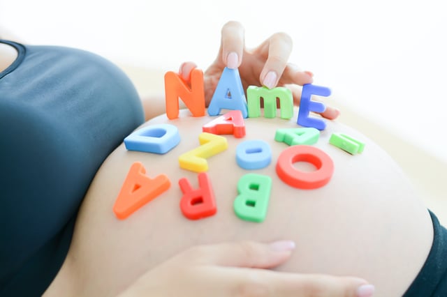 A stock image of an expectant mother with letter blocks spelling name on her pregnant belly.