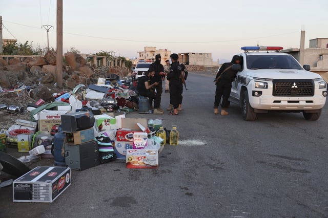 Government soldiers stand next to confiscate items stolen during clashes in Sweida city between government forces and Druze militias at a checkpoint in Mazraa village, southern Syria, Tuesday, July 15, 2025. (AP Photo/Omar Albam)