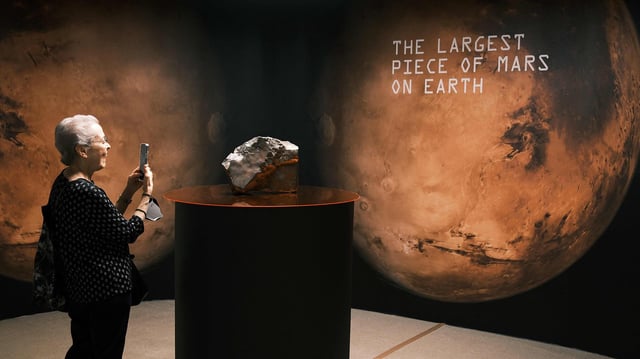 Eine Frau fotografiert den Mars-Meteoriten NWA 16788 mit einem Handy.