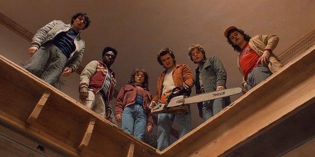 Mike Wheeler, Lucas Sinclair, Nancy Wheeler, Steve Harrington (holding a chainsaw), Jonathan Byers, and Dustin Henderson standing and looking down together in Stranger Things Season 5