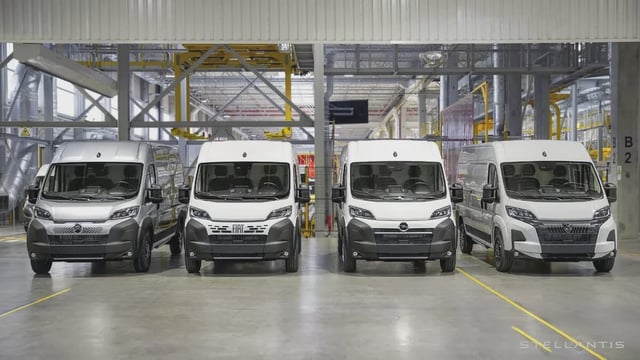 A row of four white Stellantis vans in a factory