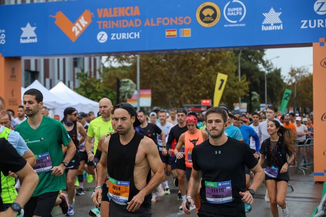 Corredores en la última media maratón de València pasan bajo el arco de salida con el patrocinio de Luanvi.