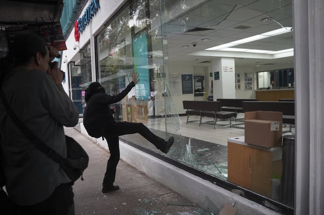 A demonstrator kicks in a bank storefront window at the end of peaceful protest that turned violent against gentrification, as the increase in remote workers has risen prices and increased housing demand in neighborhoods like Condesa and Roma, in Mexico City, Friday, July 4, 2025. (AP Photo/Aurea Del Rosario)