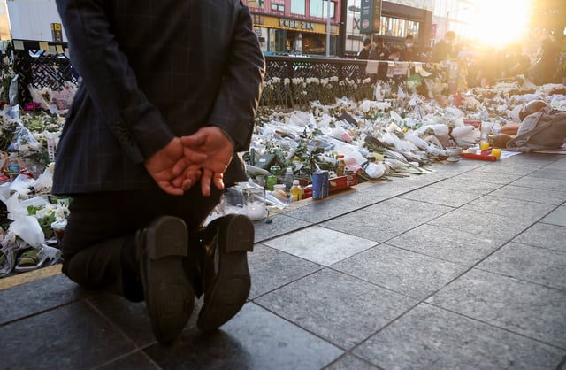 A mourner kneels next to floral tributes near the site of a crowd crush that happened during Halloween festivities, in Seoul, South Korea, November 2, 2022. REUTERS/Kim Hong-Ji/File Photo