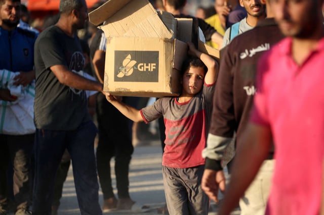 A young boy carrying an aid parcel, walks along the Salah al-Din road near the Nusseirat refugee camp in the central Gaza Strip, used by food-seeking Palestinians to reach an aid distribution point set up by the privately-run Gaza Humanitarian Foundation (GHF), on June 25, 2025.