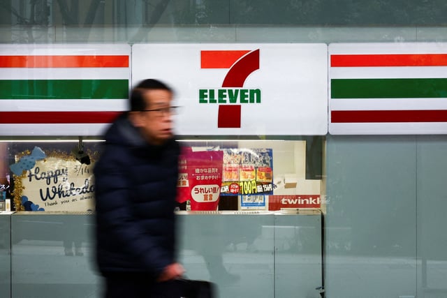 A man walks past the logo of 7-Eleven displayed at their convenience store in Tokyo, Japan March 6, 2025.