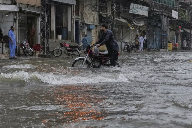 A man walks with his motorcycle through a flood road caused by heavy monsoon rains, in Rawalpindi, Pakistan, Thursday, July 17, 2025. (AP Photo/Anjum Naveed)