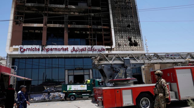 Feuerwehrleute stehen vor einem ausgebrannten Supermarktgebäude in Al-Kut, Irak. 