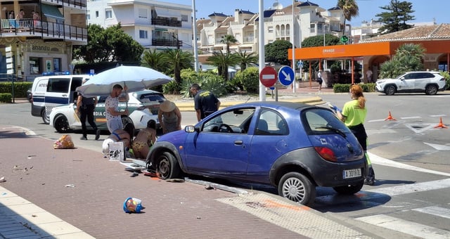El coche ha chocado luego contra un bolardo. A la izquierda y bajo la sombrilla, atienden al niño de unos 2 años que ha resultado herido