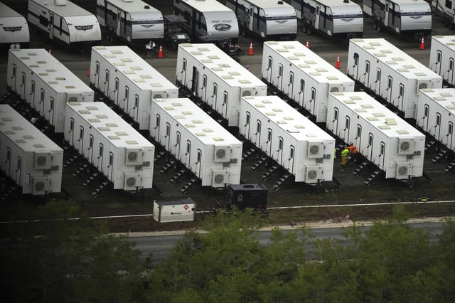 Workers sit alongside trailers as work progresses on a new migrant detention center dubbed "Alligator Alcatraz," at Dade-Collier Training and Transition facility in the Florida Everglades, Friday, July 4, 2025, in Ochopee, Fla. (AP Photo/Rebecca Blackwell)