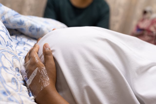 An image of a pregnant lady lying in a hospital bed holding her tummy while she waits for her cesarean section. Pregnant