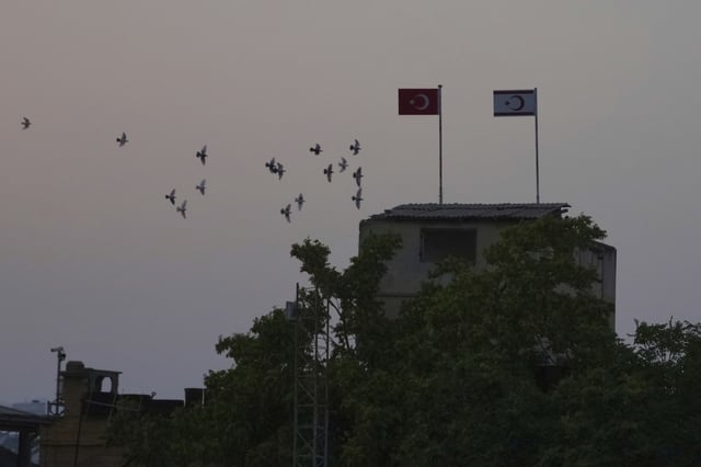 Birds fly behind a Turkish military guard post with a Turkish, left, and Turkish Cypriot breakaway flags next of a U.N buffer zone in divided capital Nicosia, Cyprus, Thursday, July 17, 2025. (AP Photo/Petros Karadjias)