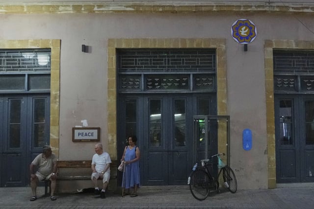 People gather at a bench near a "Peace" sign next to the main Ledra crossing point in central divided capital Nicosia, Cyprus, Thursday, July 17, 2025. (AP Photo/Petros Karadjias)