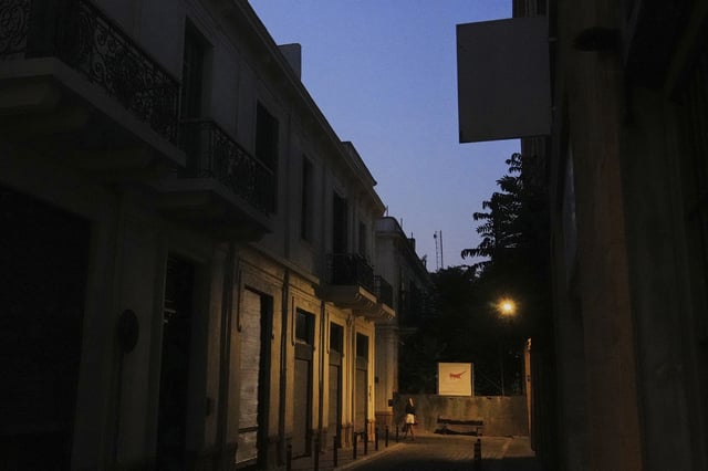 A woman walks across the U.N buffer zone in front of a blocked road as a banner shows the Cyprus island divided, the Turkish occupied area at the north and Cyprus republic at the south, in divided capital Nicosia, Cyprus, Thursday, July 17, 2025. (AP Photo/Petros Karadjias)