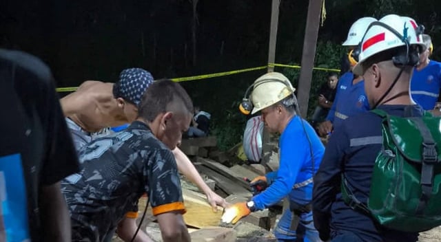 Un grupo de rescatistas y trabajadores mineros corta y mueve vigas de madera durante las operaciones de rescate tras el derrumbe en una mina ilegal en Remedios, Antioquia, Colombia. La imagen muestra un entorno nocturno con linternas y cascos de seguridad visibles.