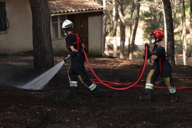 French firefighters spray water next to a house to contain a wildfire in Martigues near Marseille, France, July 18, 2025. REUTERS/Manon Cruz