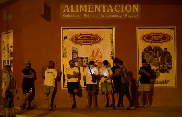Des jeunes hommes consultent leurs téléphones portables à Torre Pacheco (Espagne), le 15 juillet 2025, alors qu'un rassemblement a été appelé par des groupes d'extrême droite après quatre jours de manifestations et de violences anti-migrants