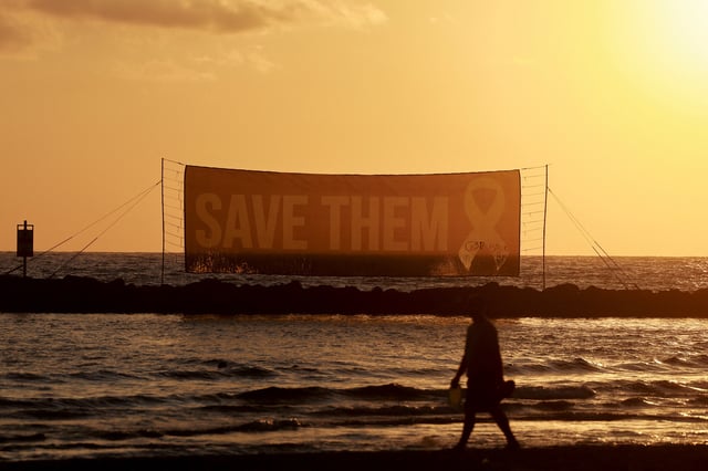 A person walks on the beach, as a sign asks for the safe return of hostages held in Gaza since October 7, 2023 attack on Israel by Hamas, near the U.S. Consulate in Tel Aviv, Israel, July 7, 2025. REUTERS/Ammar Awad/File Photo