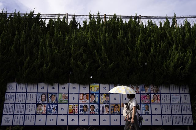 A pedestrian passes an election board displaying posters of candidates for the upcoming July 20 upper house election in Tokyo, Friday, July 18, 2025. (AP Photo/Louise Delmotte)