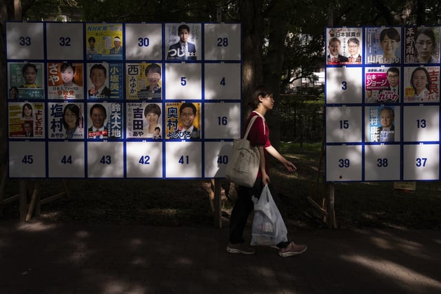 A pedestrian passes an election board displaying posters of candidates for the upcoming July 20 upper house election in Tokyo, Friday, July 18, 2025. (AP Photo/Louise Delmotte)