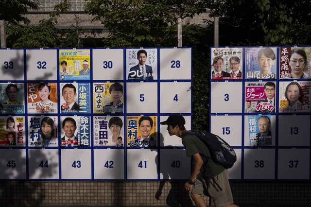 A pedestrian passes an election board displaying posters of candidates for the upcoming July 20 upper house election in Tokyo, Friday, July 18, 2025. (AP Photo/Louise Delmotte)