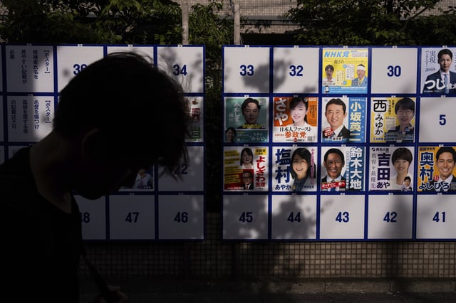 A pedestrian passes an election board displaying posters of candidates for the upcoming July 20 upper house election in Tokyo, Friday, July 18, 2025. (AP Photo/Louise Delmotte)