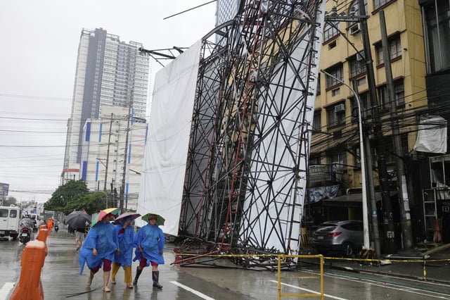 Women wearing rain gear walk beside a toppled billboard in Quezon city, Philippines due to enhanced winds and rain as Tropical Storm Wipha, locally called Crising, exits the northern portion of country on Saturday, July 19, 2025. (AP Photo/Aaron Favila)