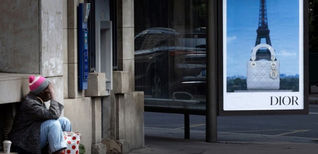 Une personne sans abri à Paris, devant une publicité pour une marque de luxe, le 8 juillet 2025