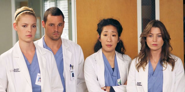 Greys Anatomy cast of characters standing with somber expressions.