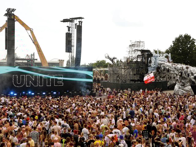 People listen to DJs Odymel and Pegassi performing at the Tomorrowland music festival in Boom, Belgium, Friday, July 18, 2025, two days after a huge fire on Wednesday severely damaged the main stage, right. (AP Photo/Omar Havana)