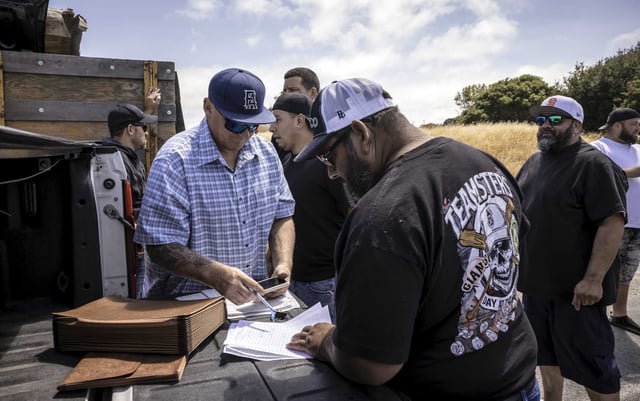 Teamsters Local 315 business agent Mike Hughes, left, dispenses benefits checks to union members outside the Golden Bear Transfer Station in Richmond on Tuesday before the tentative agreement was announced.