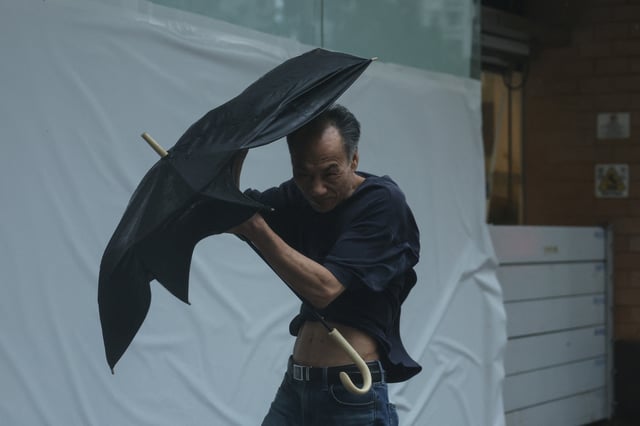 A man struggles with an umbrella while walking against strong wind, as Typhoon Wipha approaches, in Hong Kong, China, July 20, 2025. REUTERS/Tyrone Siu