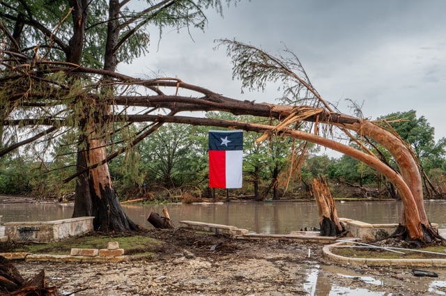 A Texas flag hangs from a storm-damaged tree on the banks of the Guadalupe River on July 13, 2025 in Center Point, Texas. More than 160 people are still missing after storm cells halted over the area, dumping nearly 15 inches of rain and causing a 22-foot rise along the Guadalupe River.