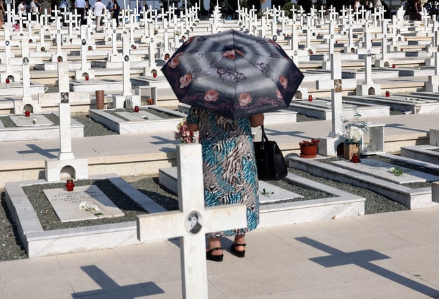 A woman walks next to the graves of soldiers killed in the 1974 Turkish invasion of Cyprus at the Tymvos Makedonitissas military cemetery in Nicosia, Cyprus July 20, 2025. REUTERS/Yiannis Kourtoglou