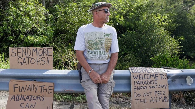Marc Ribas sits outside of Alligator Alcatraz with his signs and a custom shirt on July 12, 2025, in Ochopee, Florida. (Luis Santana/Tampa Bay Times/TNS)