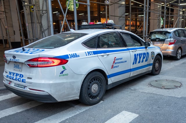 NYPD hybrid patrol car parked alongside a street lined with scaffolding near a Starbucks, New York City, New York, October 20, 2024.
