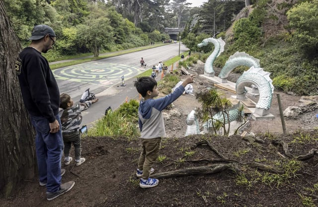 James Mitchell, left, and his sons, Theo, 2, and Jay, 4, stop on a hillside to admire the Naga sea serpent sculpture in Golden Gate Park.