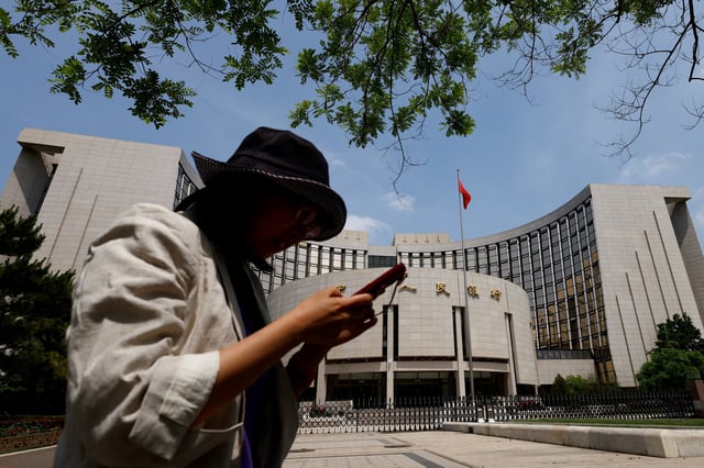 A woman uses phone as she walks past the headquarters of the People's Bank of China, in Beijing, China May 7, 2025. REUTERS/Tingshu Wang/File Photo