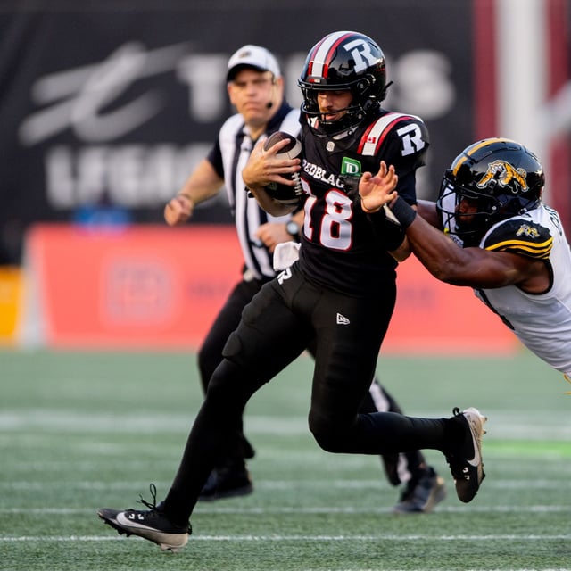 Ottawa Redblacks quarterback Dustin Crum (18) is sacked by Hamilton Tiger-Cats defensive lineman TyJuan Garbutt (9) during first half CFL action in Ottawa on Sunday, July 20, 2025. THE CANADIAN PRESS/Spencer Colby