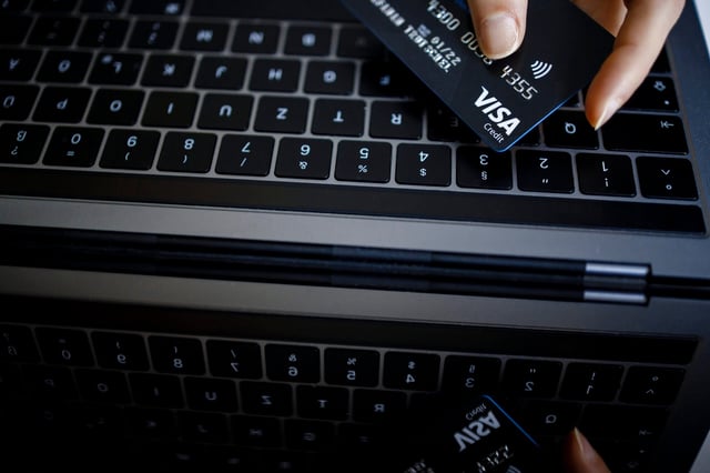 BERLIN, GERMANY - FEBRUARY 02: Symbolic photo on the subject of online shopping. A VISA credit card is held next to the keyboard of a laptop. (Photo by Thomas Trutschel/Photothek via Getty Images)