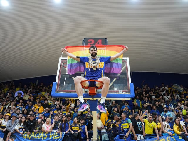 Sebastián Vega, con la bandera de la comunidad LGBT+ colgado del aro después de consagrarse bicampeón de la Liga Nacional con Boca.