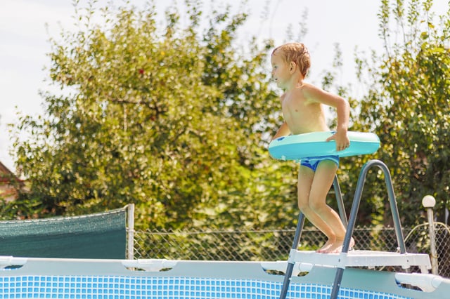Stock image of a child jumping off a ladder into an above-ground pool.