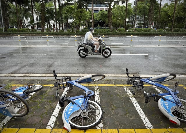 A motorcyclist drives past fallen bicycles in the rain caused by tropical storm Wipha in Hanoi, Vietnam on Tuesday, July 22, 2025. (AP Photo/Huy Han)