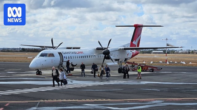 Passengers get off a small Qantas plane on the tarmac at a small airport.