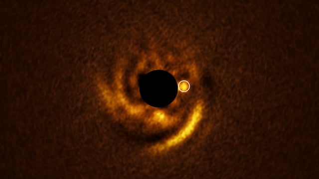 Astronomers believe the spiral disk in this photograph may be evidence of a planet forming around the young star HD 135344B. The location of this potential planet is indicated with a white circle. The central black circle corresponds to a coronagraph — a device that blocks the star's light to reveal details around it.