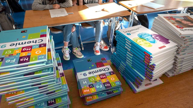Schulbücher liegen auf einem Tisch in einem Klassenzimmer.