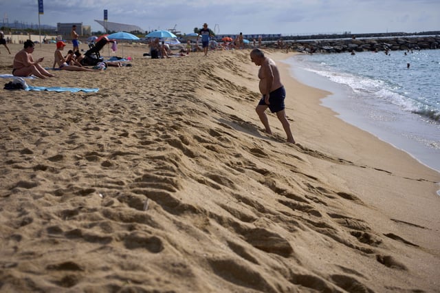A swimmer walks on the shore of a beach in Barcelona, Spain, Tuesday, July 22, 2025. (AP Photo/Emilio Morenatti)