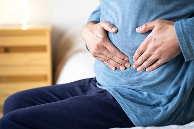 Man sitting on bed holding stomach in pain.