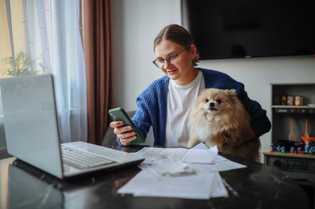 middle-aged woman in glasses with a laptop and papers works with her pet spitz dog at a table at home, taxes and financial home organization